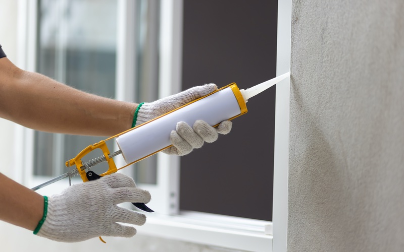 A person caulking a window frame, WyattWorks Charlotte.