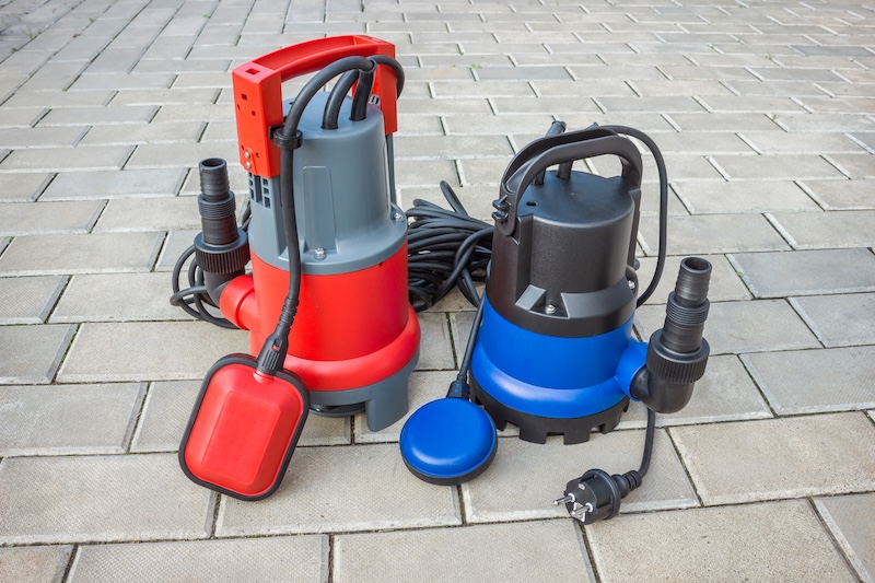 An image of two sump pumps sitting on a driveway - call WyattWorks for sump pump and sewer services in Ohio & North Carolina, {fran_state_abbrev}.